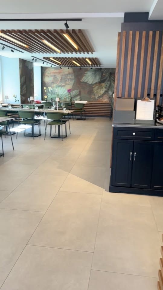 Ein modernes Café-Interieur mit hellen Fliesenböden, grünen Stühlen, Tischen und Holzlamellen an der Decke.