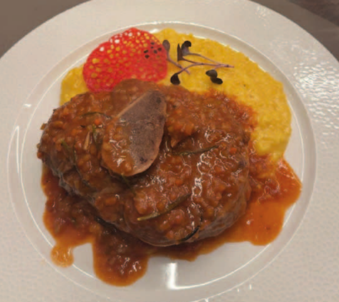 Eine Portion geschmortes Ossobuco mit roter Sauce, serviert zusammen mit leuchtend gelbem Safranrisotto auf einem weissen Teller.