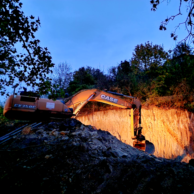 Excavateur orange creusant dans une colline au crépuscule.