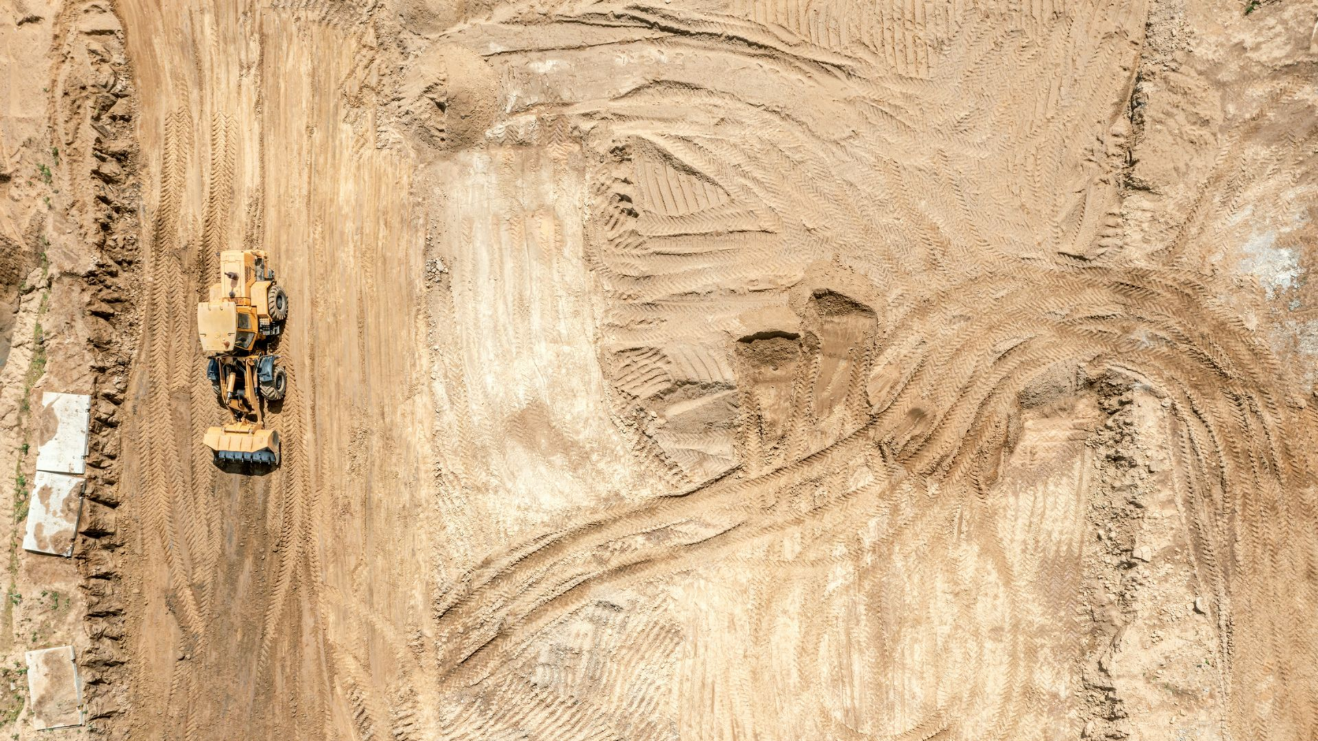 Vue aérienne d'un chantier de construction avec bulldozer et engins de terrassement, créant un chemin sur terre brune.