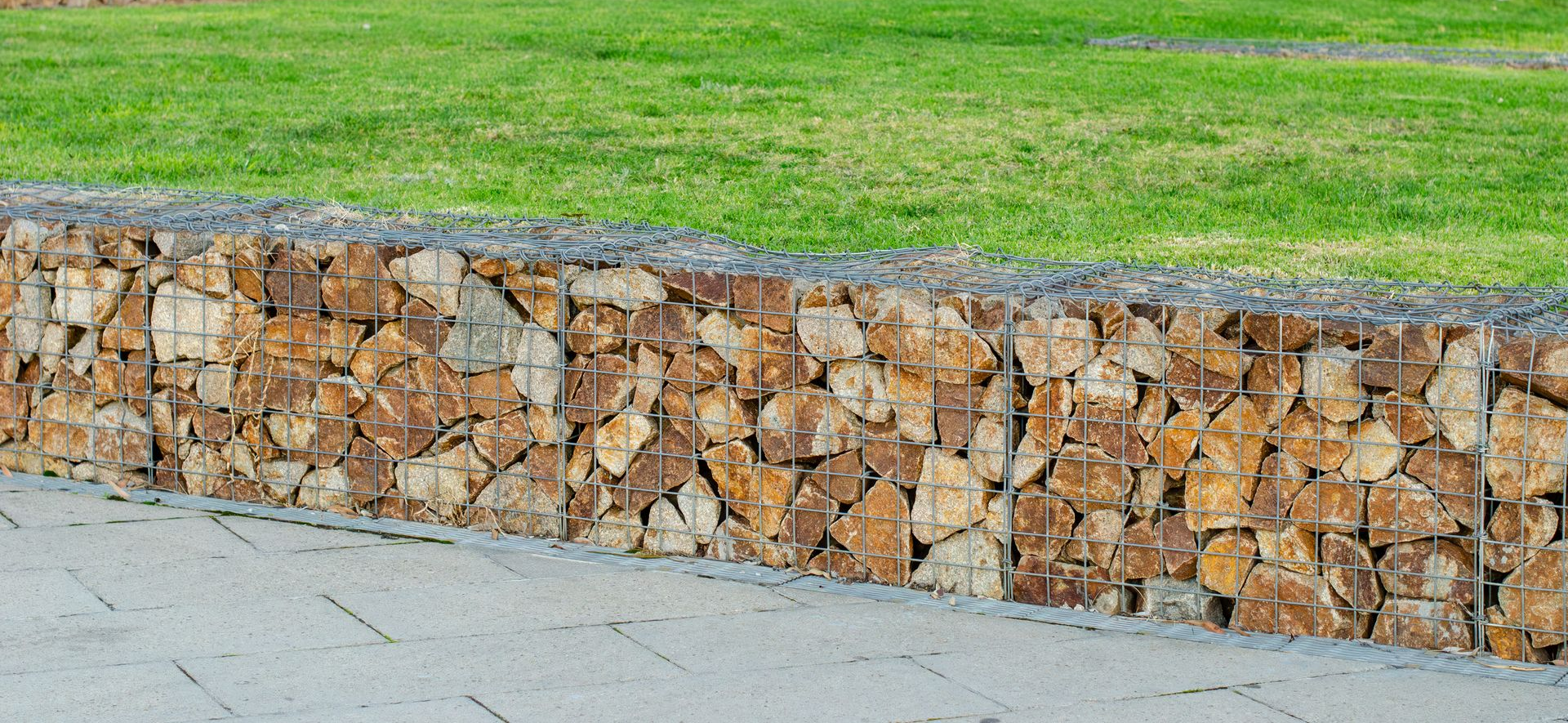 Un mur de soutènement en pierre avec une zone herbeuse derrière et un trottoir devant.