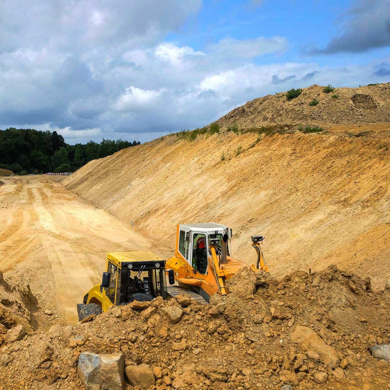Deux bulldozers creusent dans une grande carrière de sable sous un ciel nuageux.