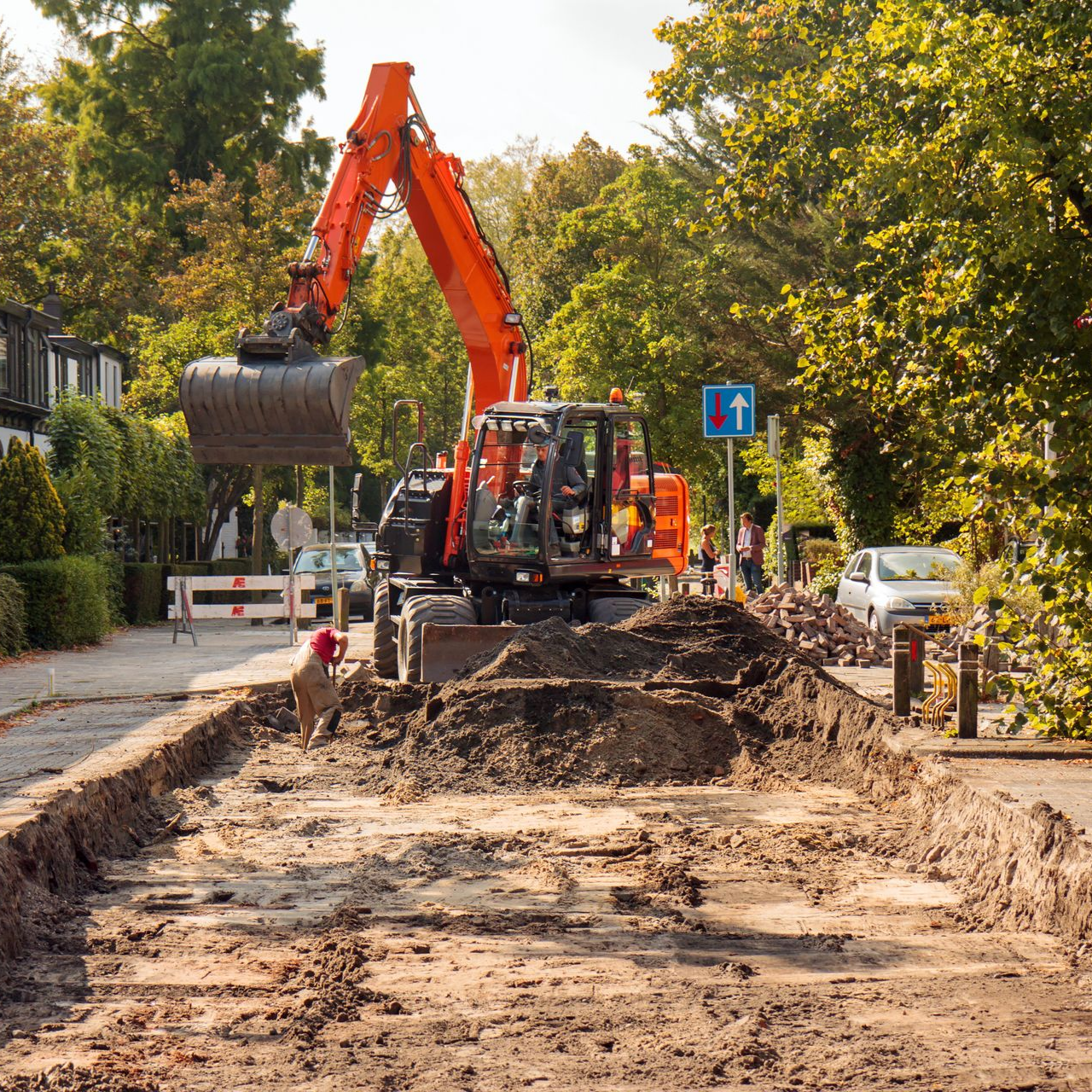 Une excavatrice creuse une tranchée dans une rue résidentielle. Un chien se tient près du sol.