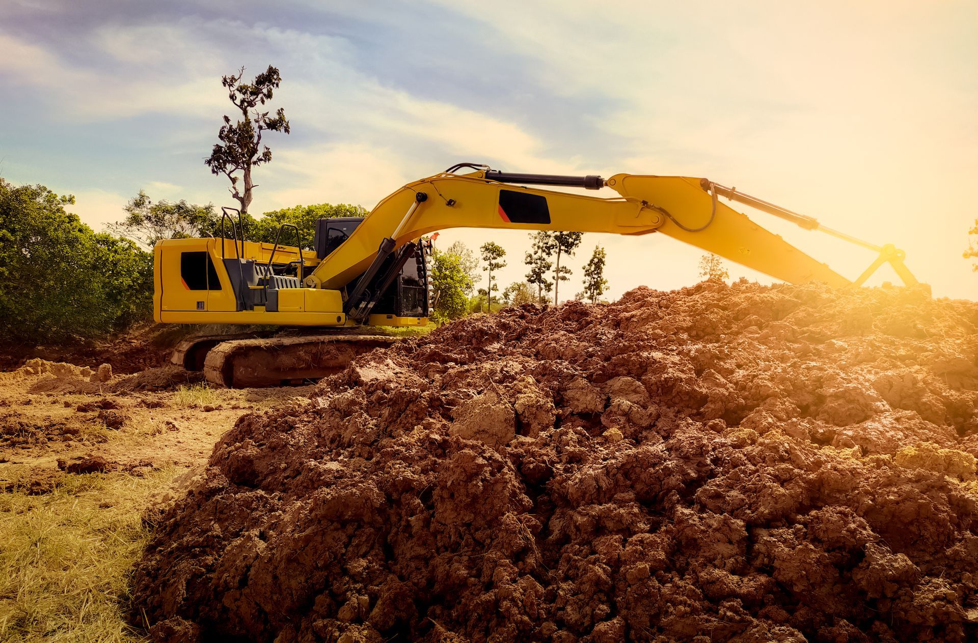 Excavateur jaune déplaçant le sol sous la lumière du soleil.