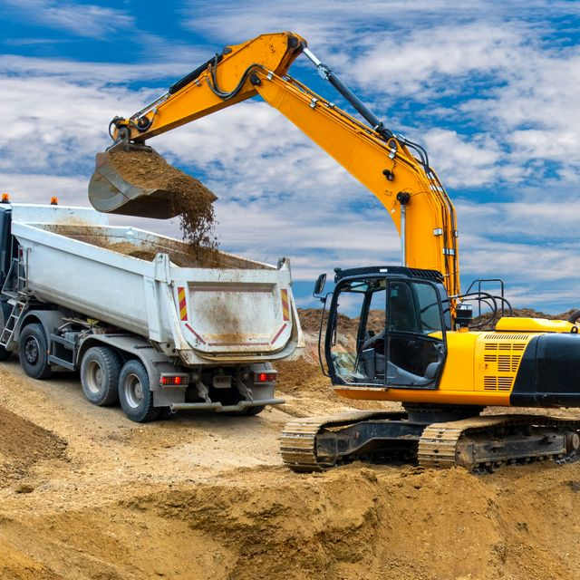 Excavatrice jaune chargeant de la terre dans un camion à benne basculante blanc, chantier de construction, ciel bleu.