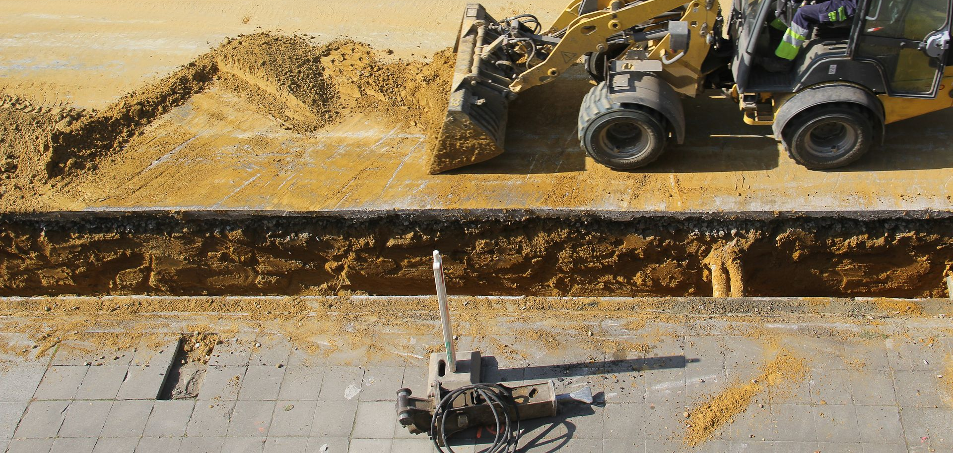 Un engin de chantier jaune creuse une tranchée par une journée ensoleillée. Un engin est installé à l'intérieur de la tranchée.