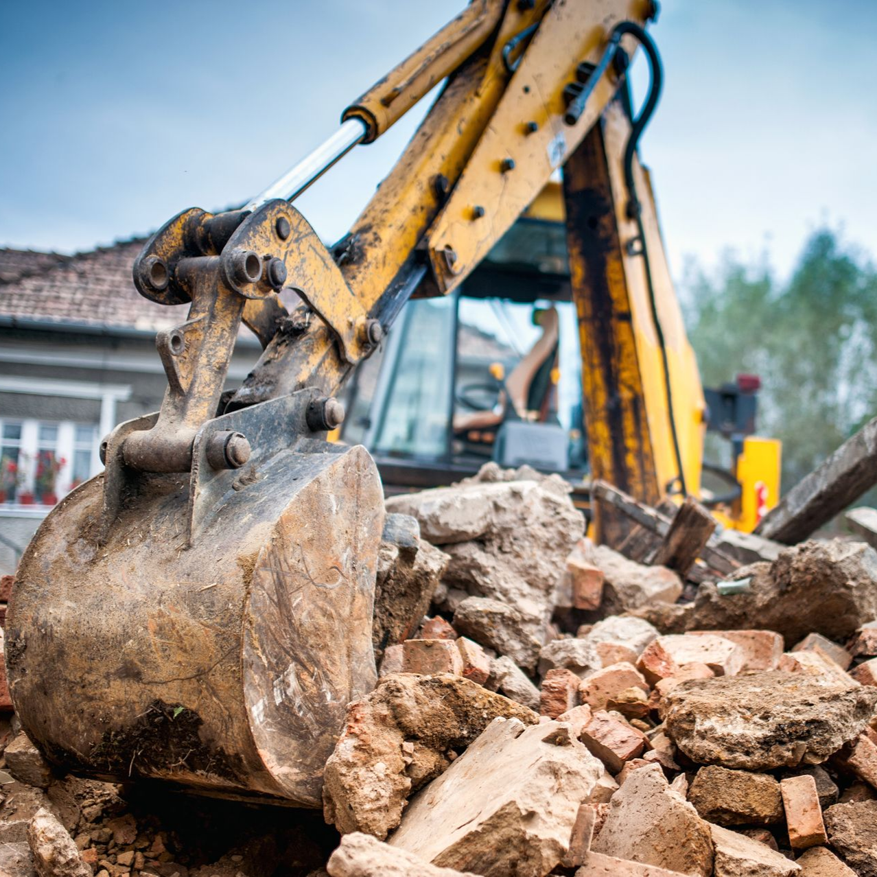Godet d'excavatrice jaune récupérant des débris sur un chantier de démolition.