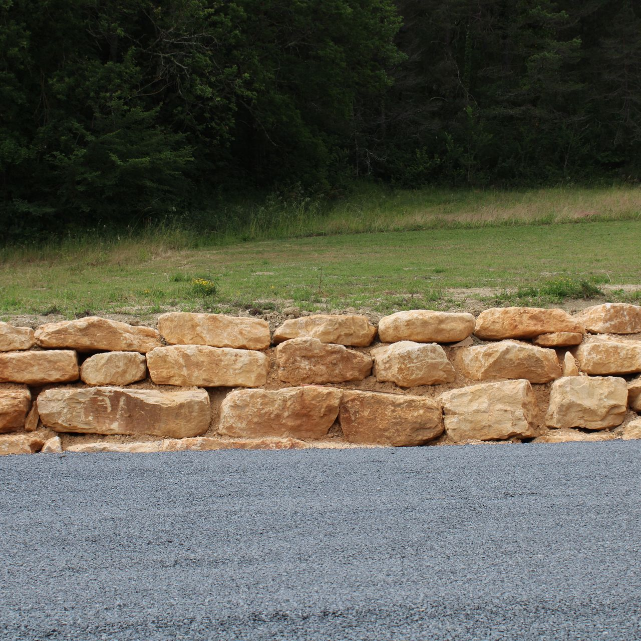 Mur de soutènement en pierre avec une base en gravier et un fond herbeux.