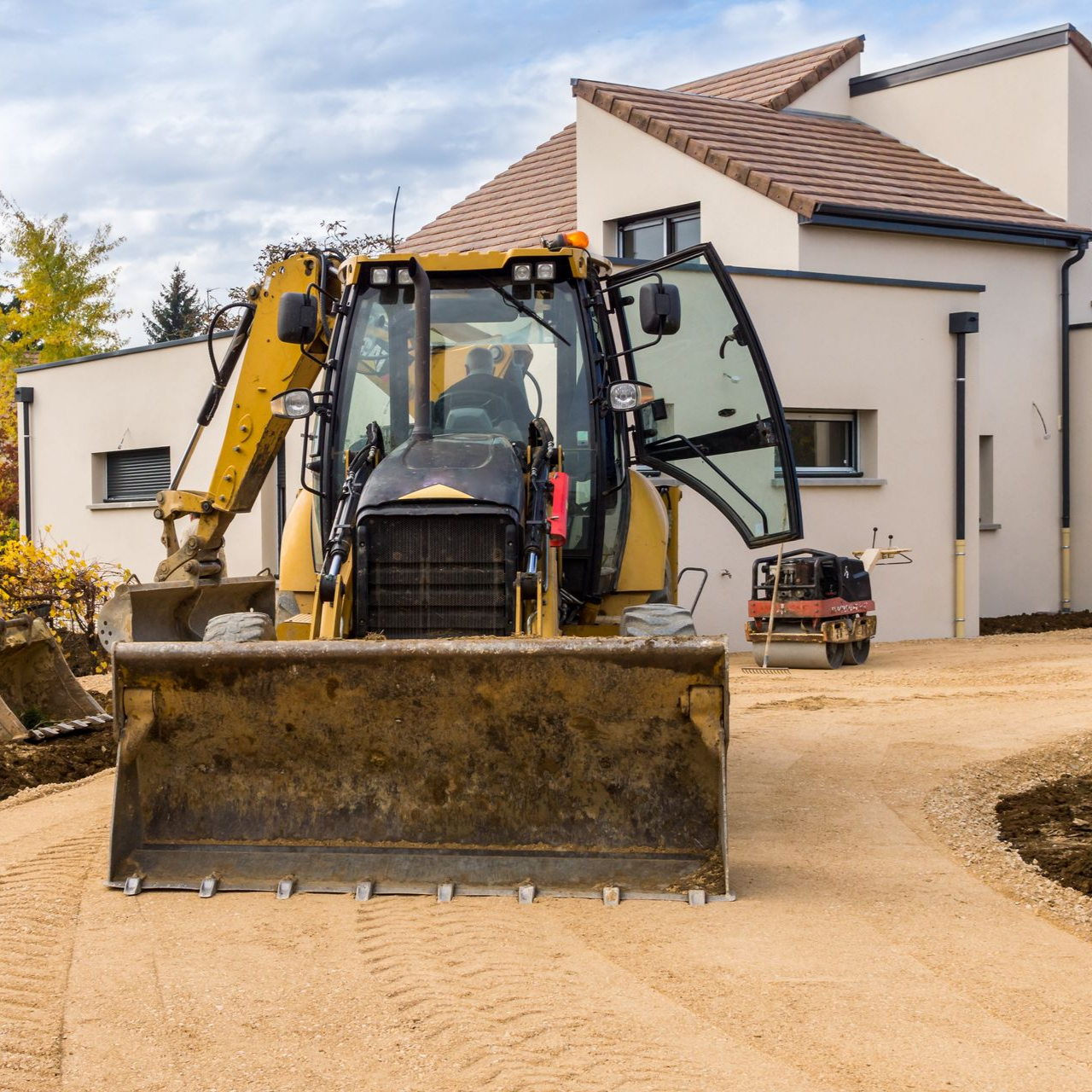 Rétrocaveuse jaune sur une allée de gravier devant une maison moderne.