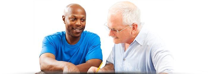 Deux hommes souriants et discutant autour d'une table, l'un en chemise bleue et l'autre en chemise bleu clair.