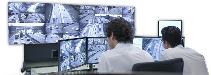 Un opérateur de sécurité surveille les flux vidéo de plusieurs caméras de surveillance sur de grands écrans dans une salle de contrôle.