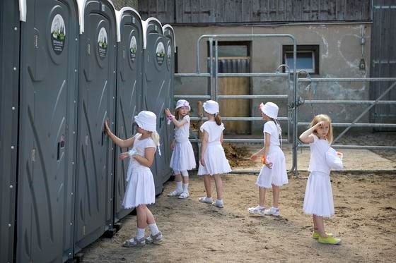 Eine Gruppe blauer Mobiltoiletten steht auf einem Gehweg neben einem Lastwagen.