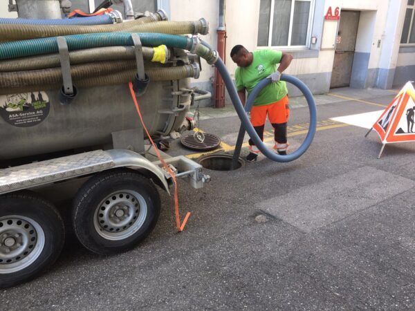 Ein Mann pumpt einen Schlauch in einen Kanaldeckel