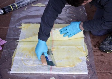 Ein Mann mit blauen Handschuhen verwendet einen Spatel auf einem Stück Papier.