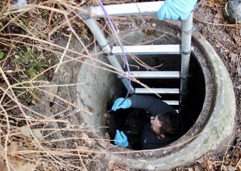 Ein Mann benutzt eine Leiter, um aus einem Gullydeckel herauszukommen.