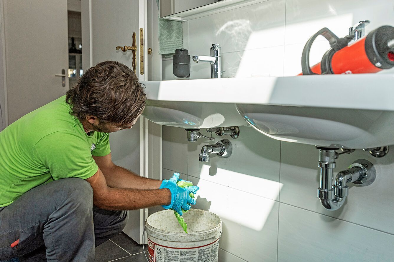 Ein Mann kniet unter einem Waschbecken in einem Badezimmer.