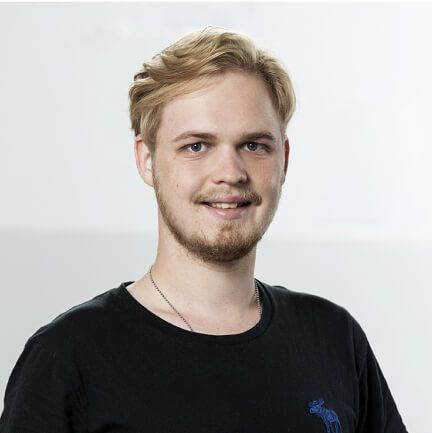 Ein junger Mann mit Bart trägt ein schwarzes T-Shirt und lächelt.