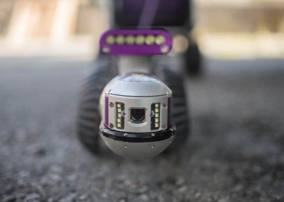 Auf dem Boden sitzt ein Roboter mit einer Kamera.