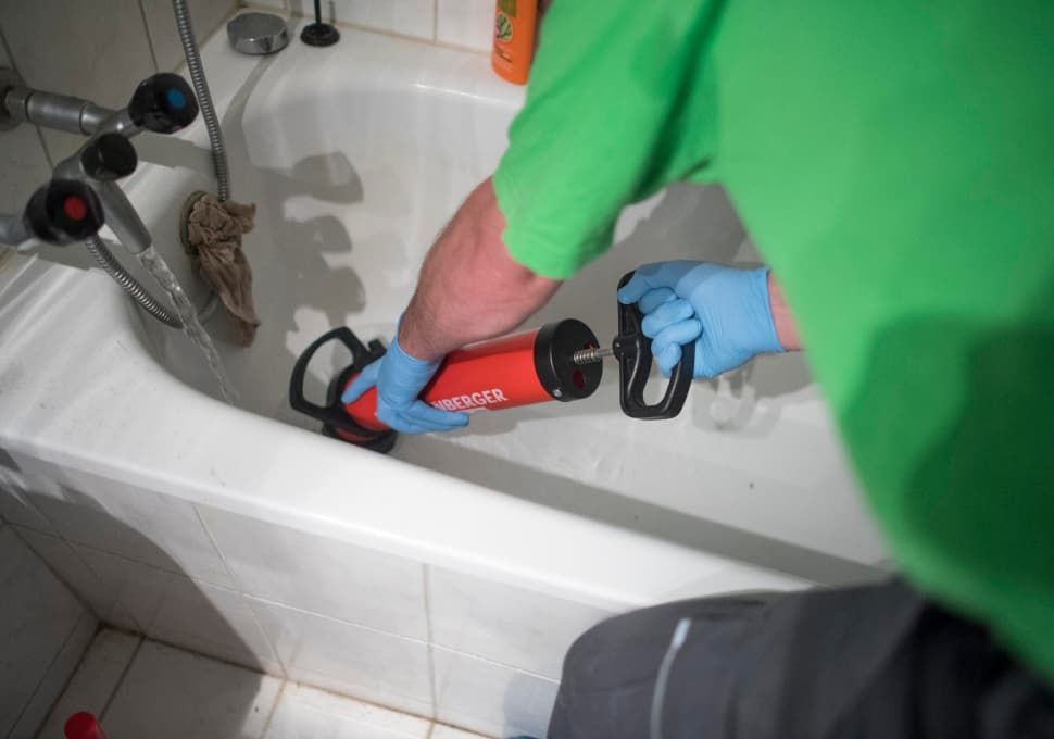 Ein Mann in einem grünen Hemd reinigt eine Badewanne mit einem Pömpel.