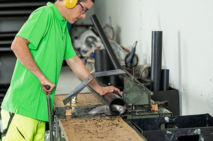 Ein Mann in einem grünen Hemd schneidet mit einer Säge ein Rohr durch.