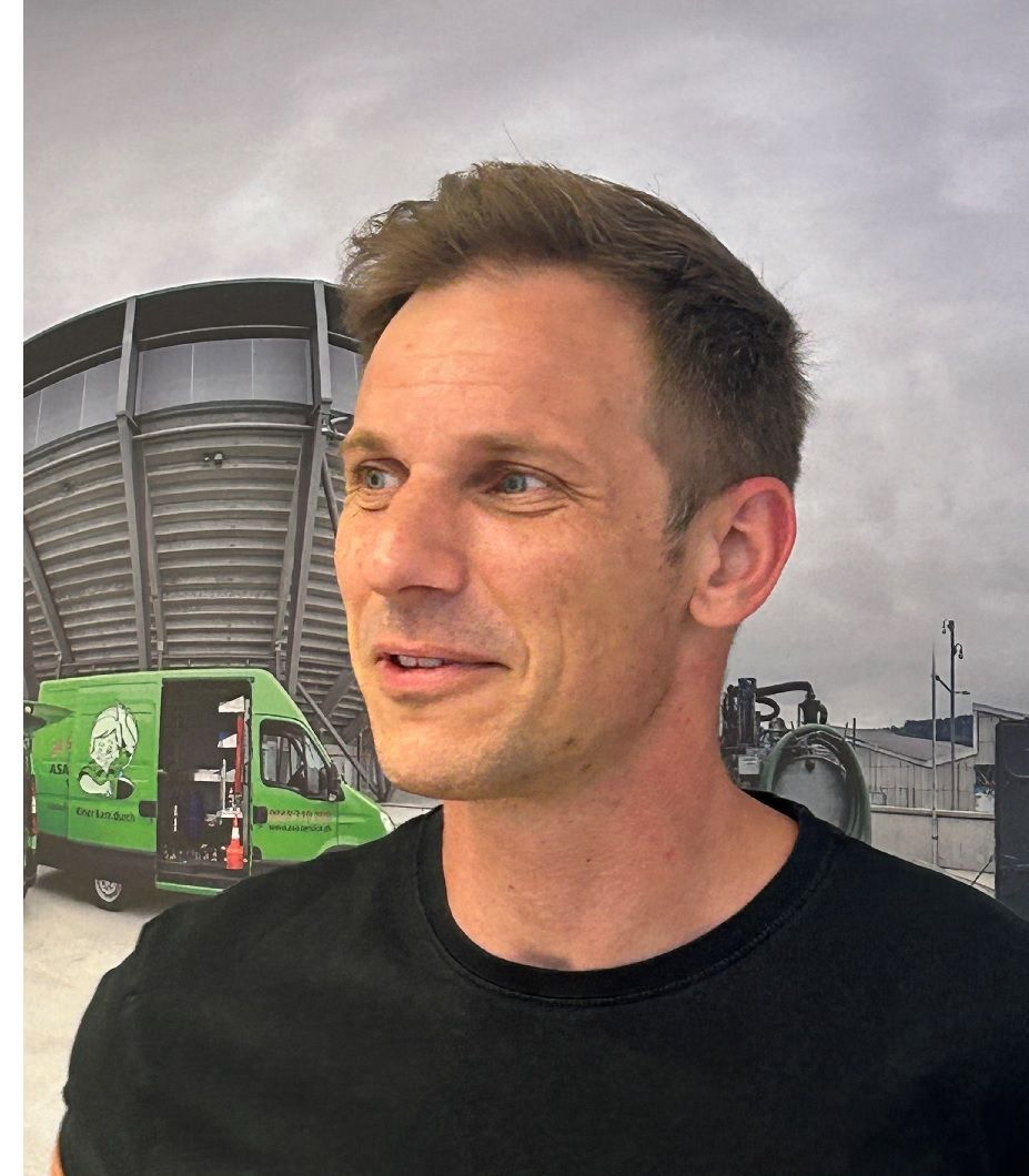 Ein Mann mit Bart steht vor einer Wand aus Metallrohren.