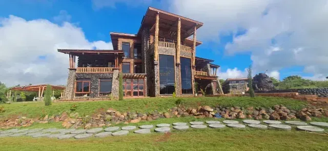 Stone-and-wood house with a tall central tower on a grassy hillside under a blue sky