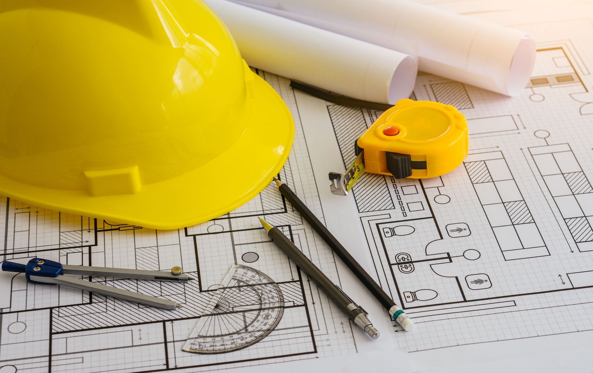 Yellow hard hat, rolled blueprints, and measuring tools on construction plans