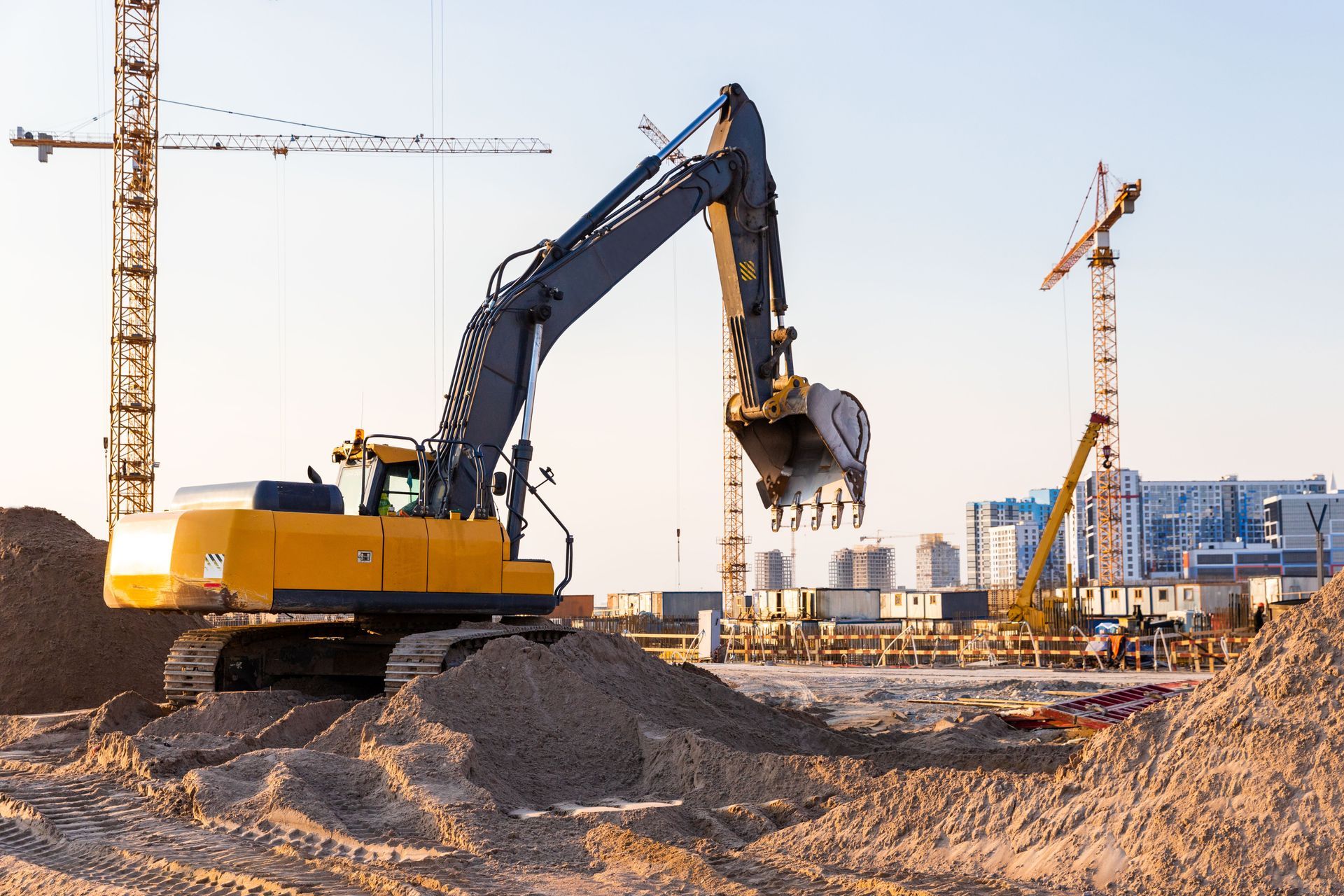 Yellow excavator lifting debris at a construction site with cranes in the background