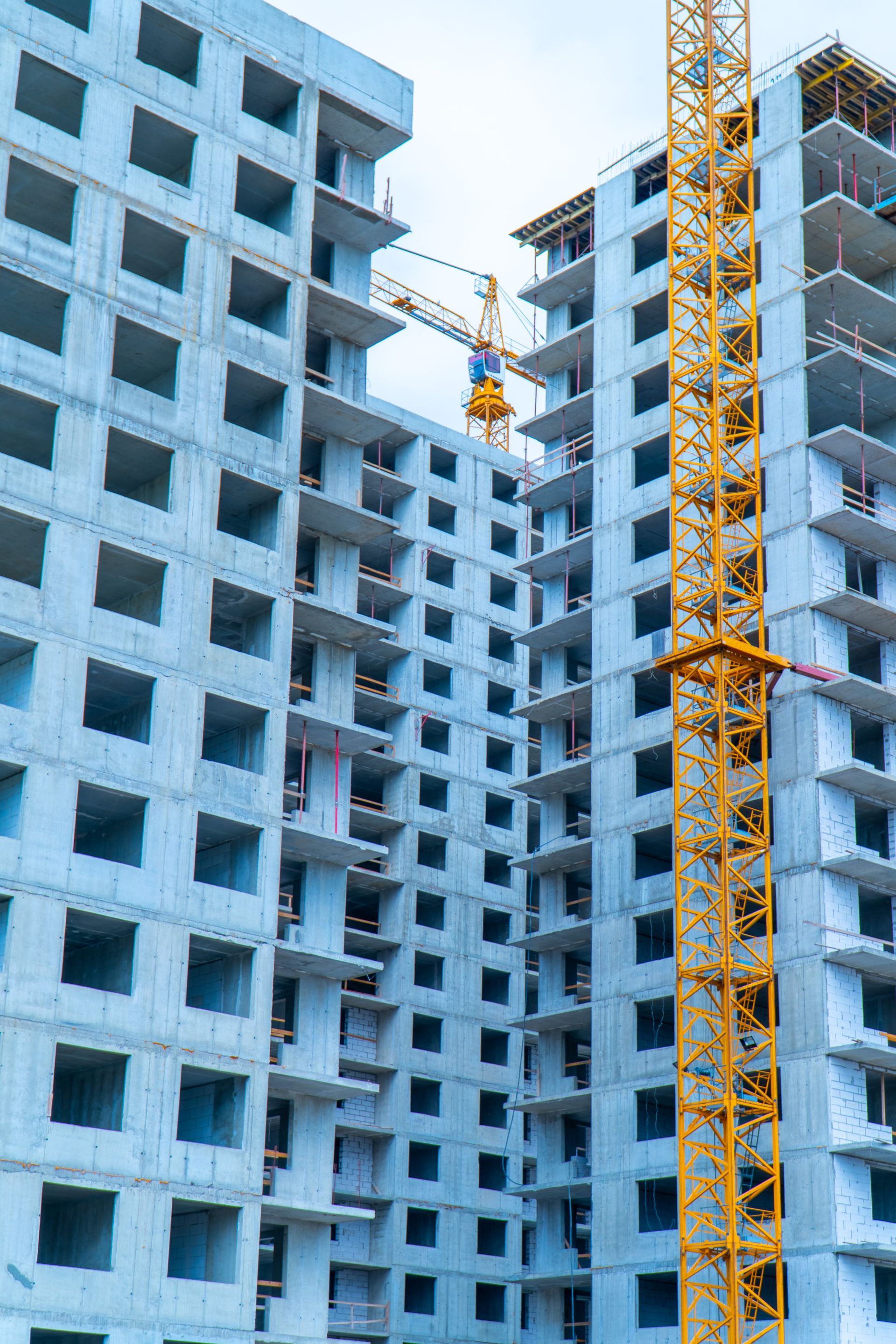 Blue high-rise apartment buildings under construction with a yellow tower crane.