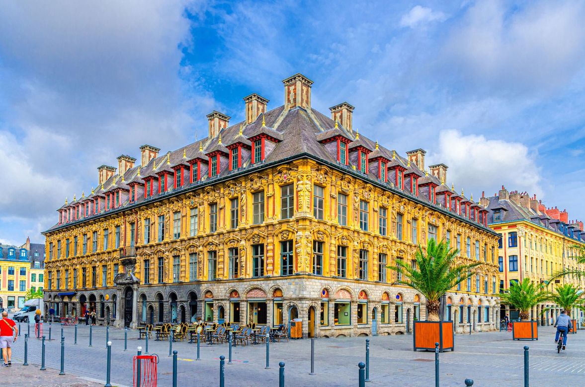 Bâtiment en briques jaunes et rouges à Lille, en France, avec un angle droit et une terrasse de café.