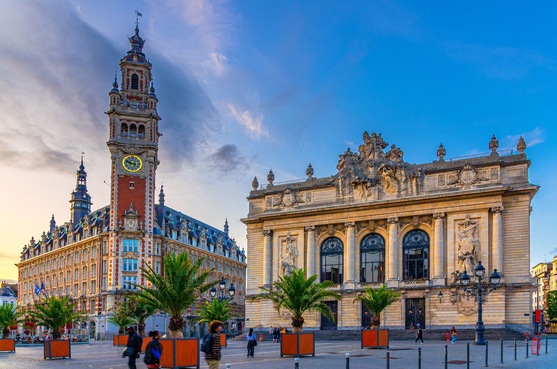 Tour de l'horloge et bâtiment orné à Lille, en France. Ciel bleu, palmiers, passants.