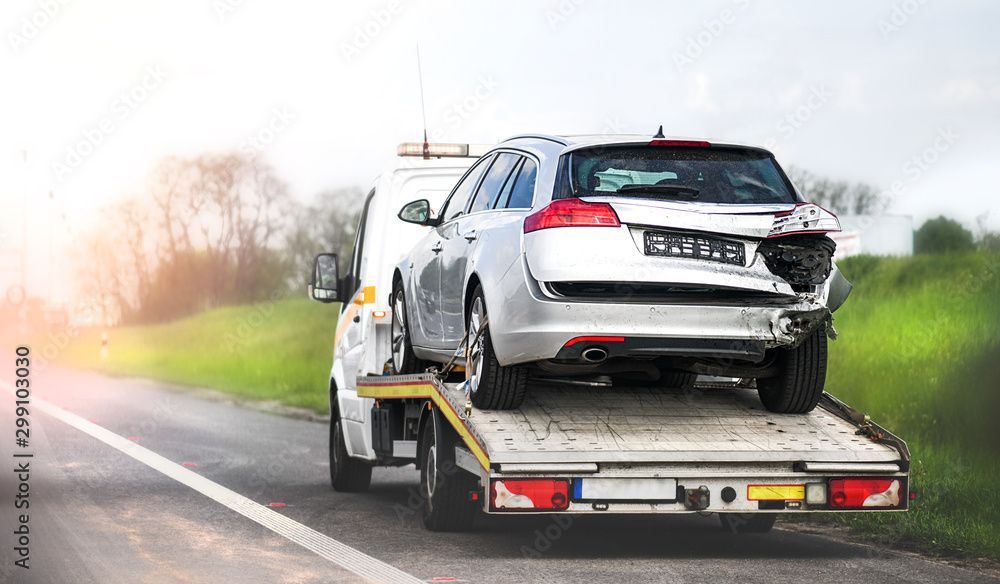 Ein beschädigter silberner Kombi wird auf der Ladefläche eines Abschleppwagens über eine Strae transportiert.