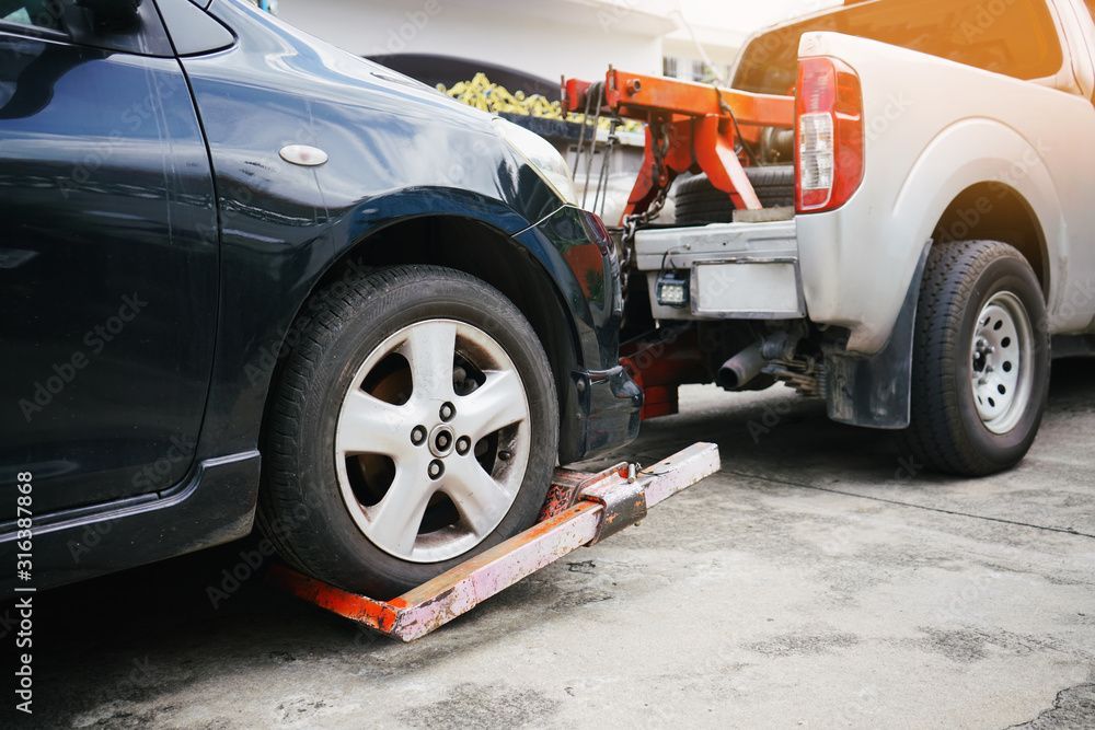 Ein schwarzes Auto wird mithilfe eines Radhebers von einem Abschleppwagen auf einer Betonfläche angehoben.
