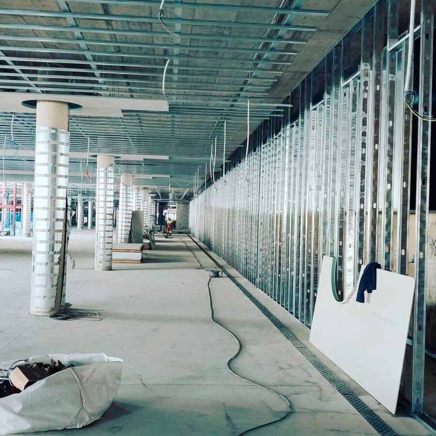 Interior de una obra en construcción; estructura metálica para paredes y techo. Suelos y columnas grises, pasillo largo.