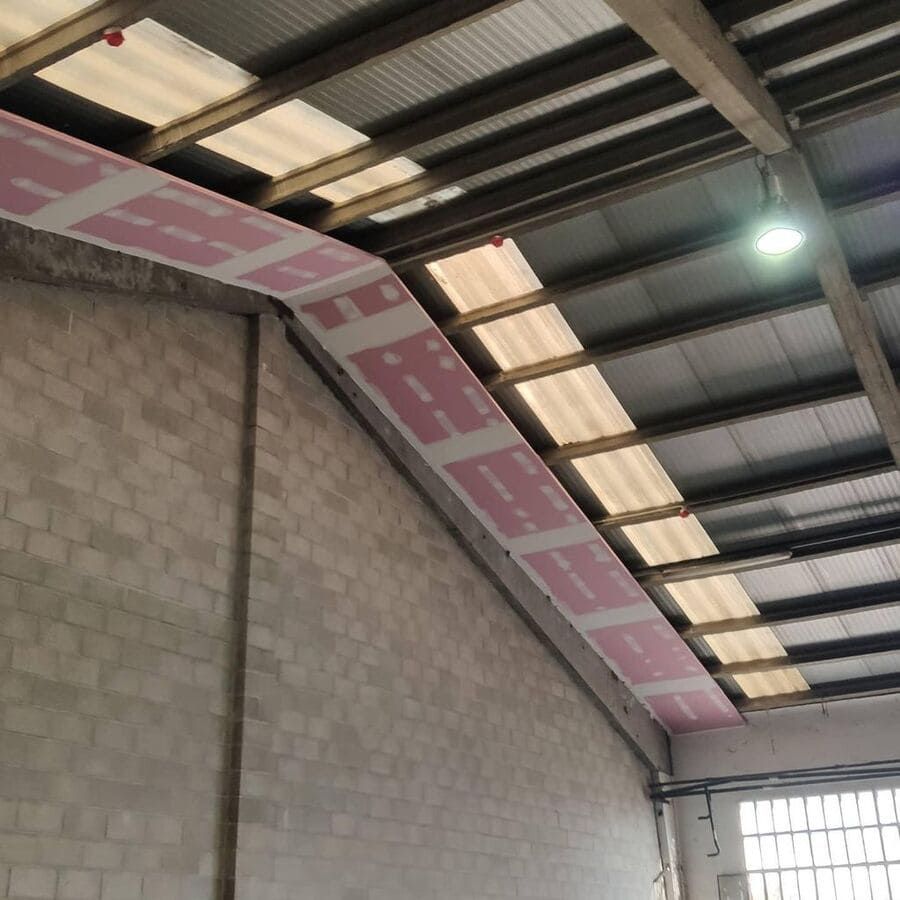 Interior de un edificio con una pared de bloques de hormigón y una sección de panel de yeso rosa que corre a lo largo del techo.