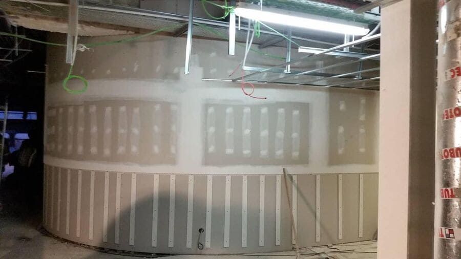Sitio de construcción: Pared de yeso curva con secciones empotradas, estructura del techo visible.