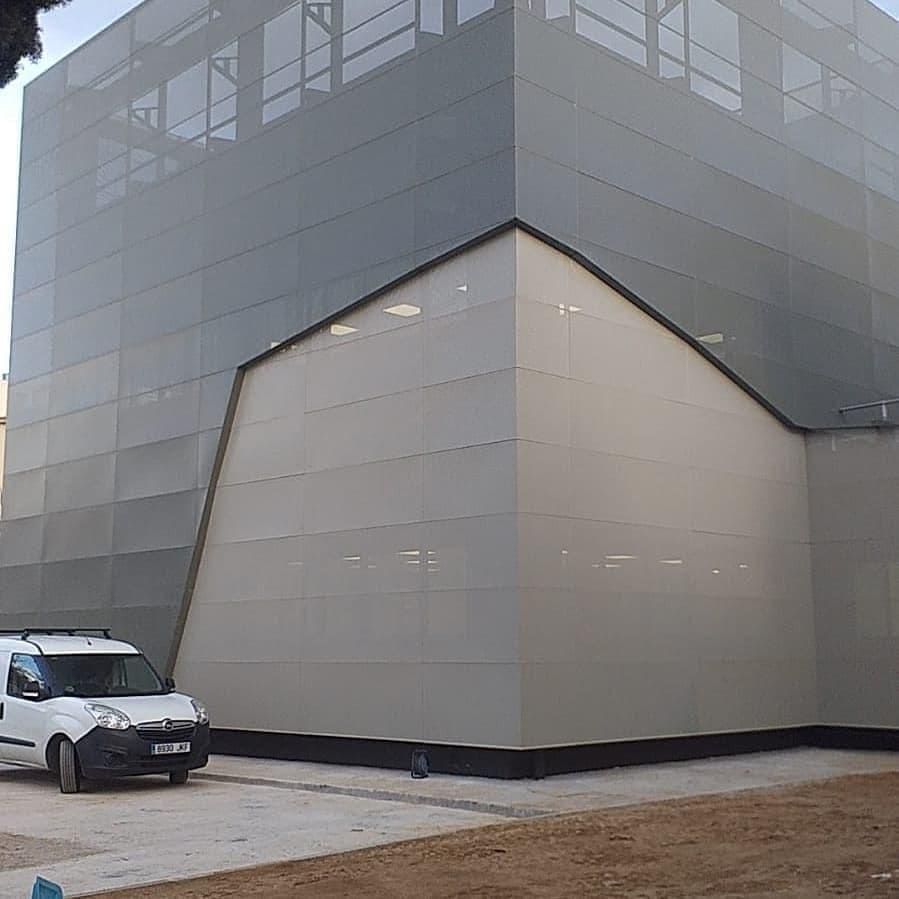 Fachada de edificio gris y blanca con una furgoneta estacionada delante.