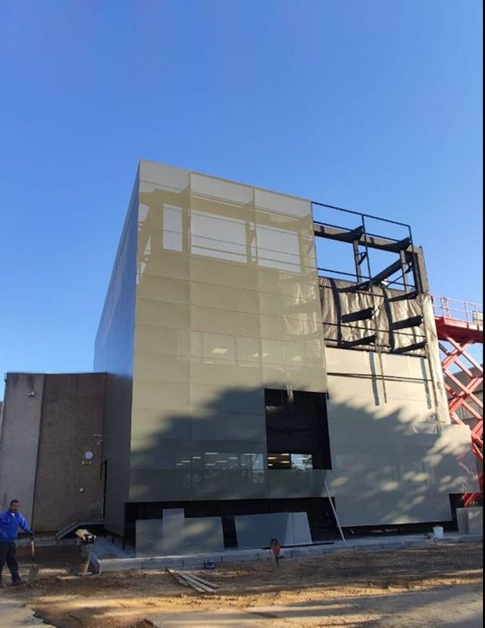 Edificio en construcción con fachada de pantalla gris y estructura de acero vista.