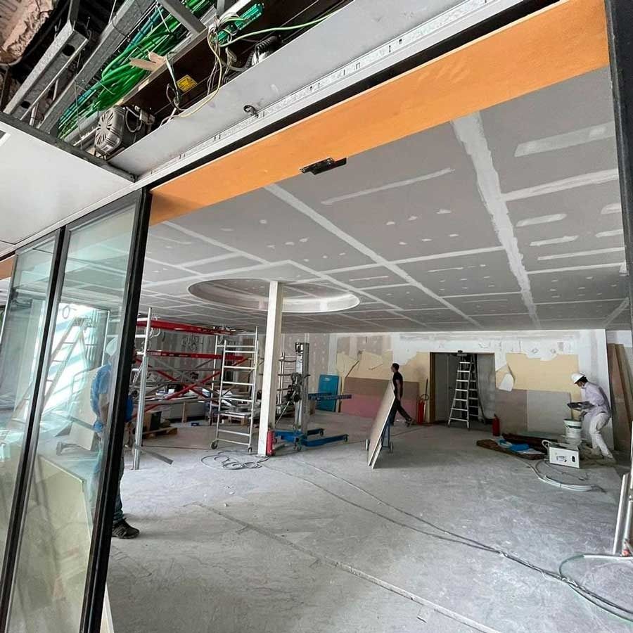 Obra interior: techos de yeso, andamios, trabajadores, herramientas y cableado expuesto.