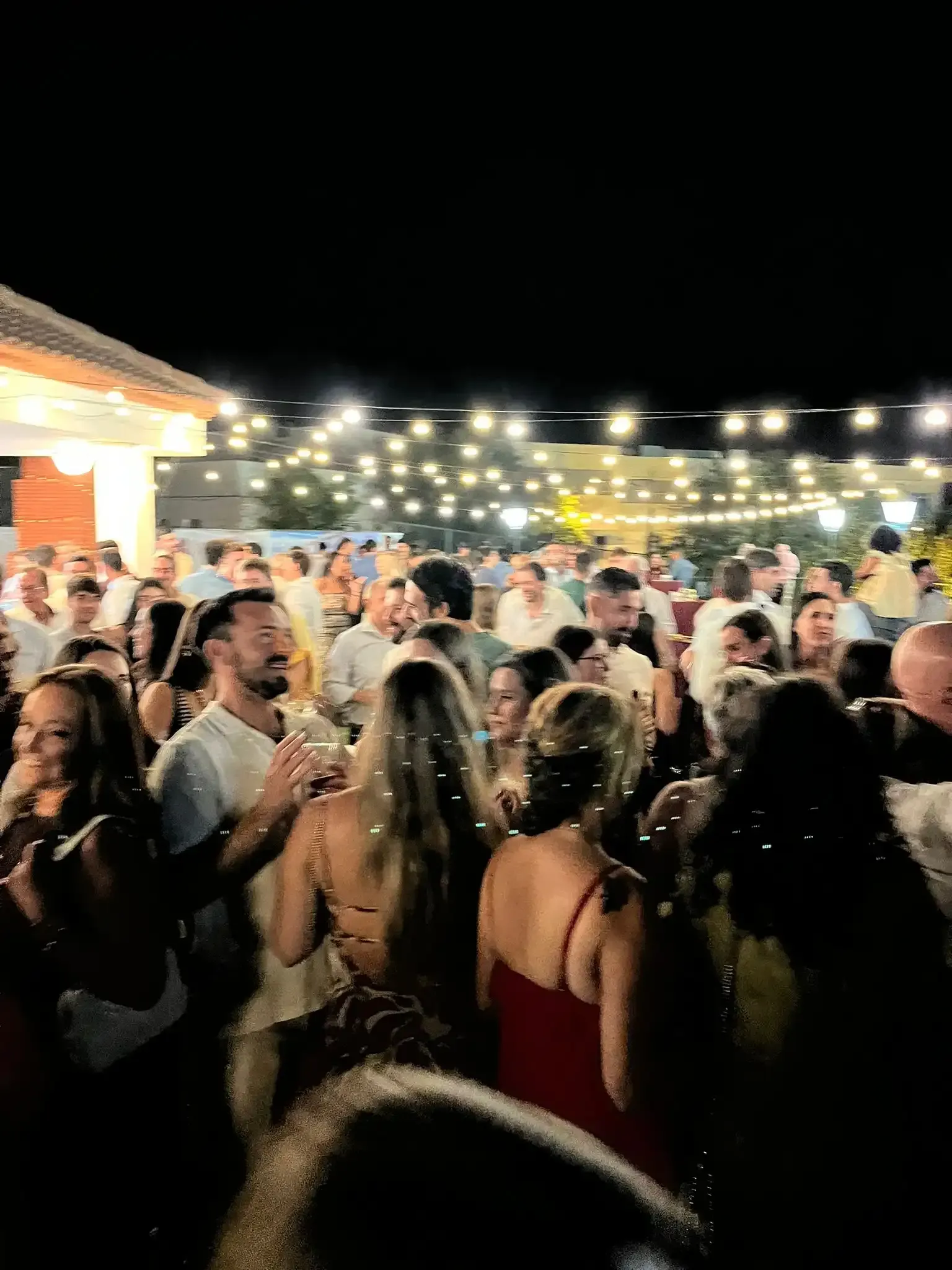 Fiesta nocturna, mucha gente, luces de colores, algunos bailando y otros hablando.