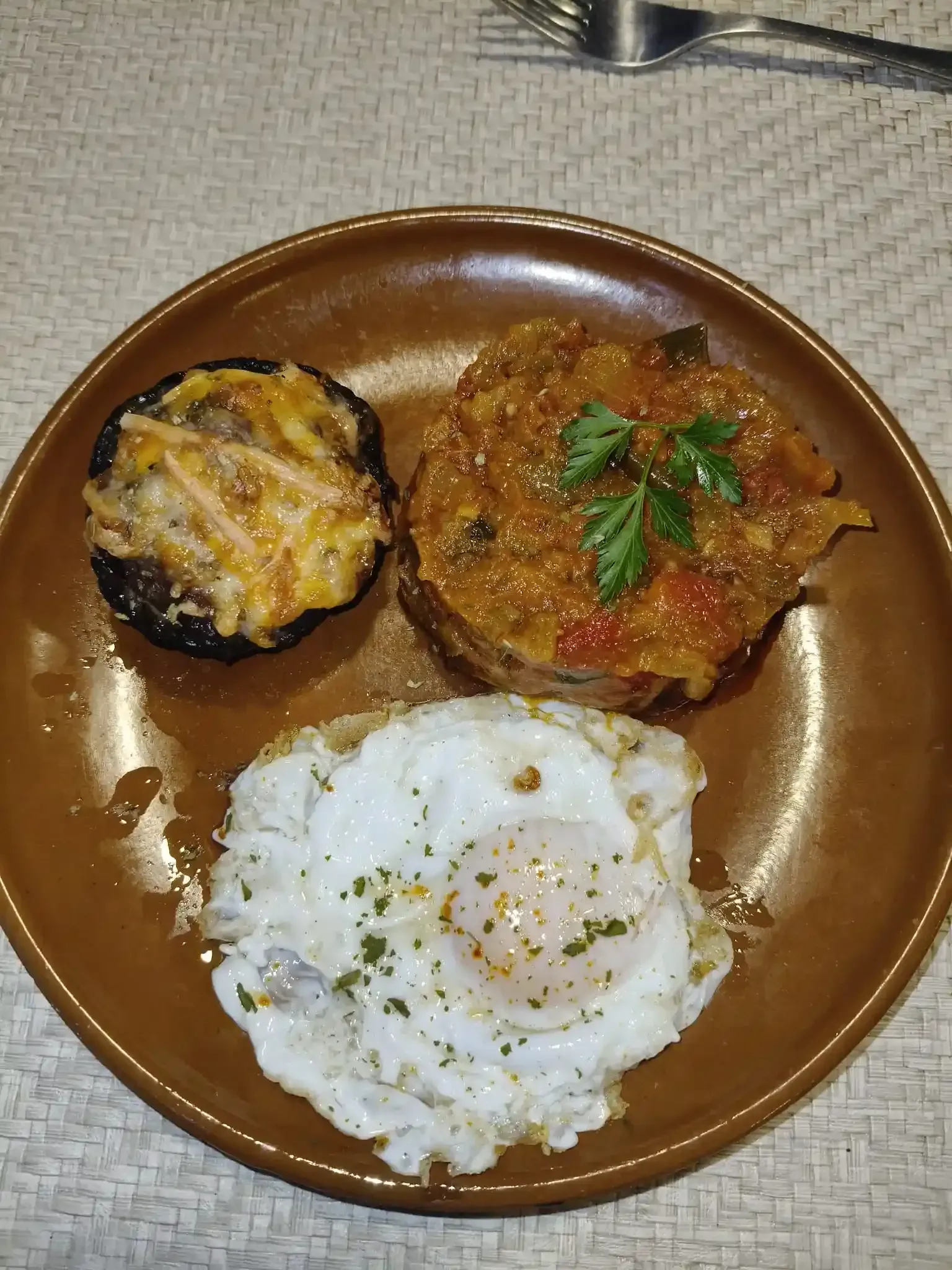 Plato marrón con un champiñón relleno, un pastel de verduras y un huevo frito.