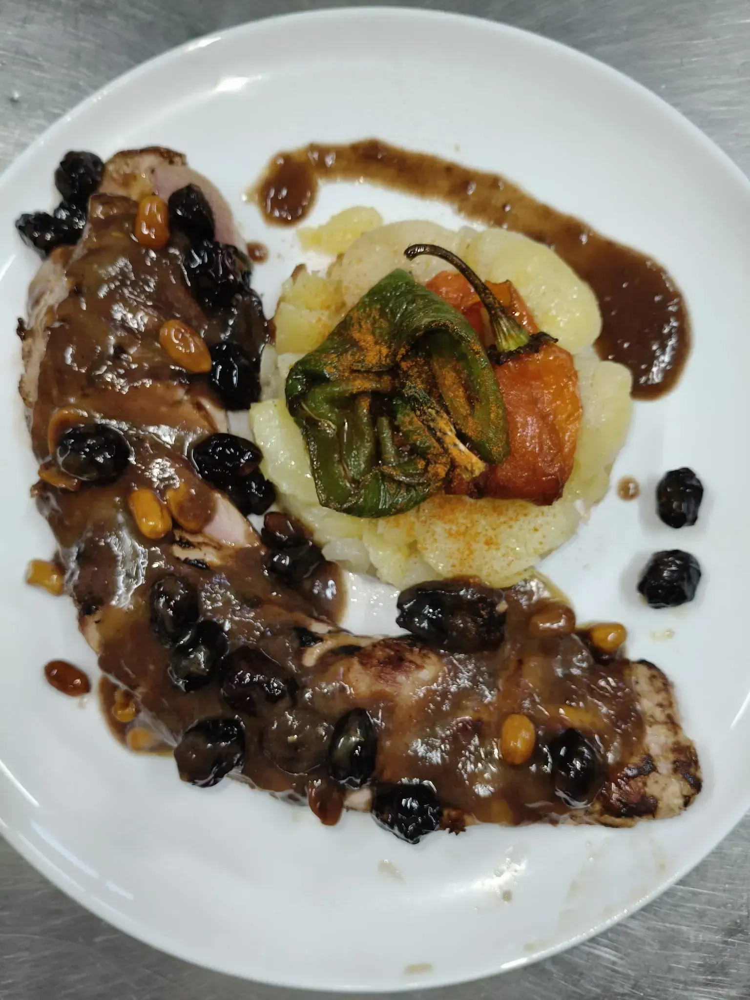 Solomillo de cerdo con salsa, frutos secos y nueces, servido con patatas asadas y pimientos en un plato blanco.