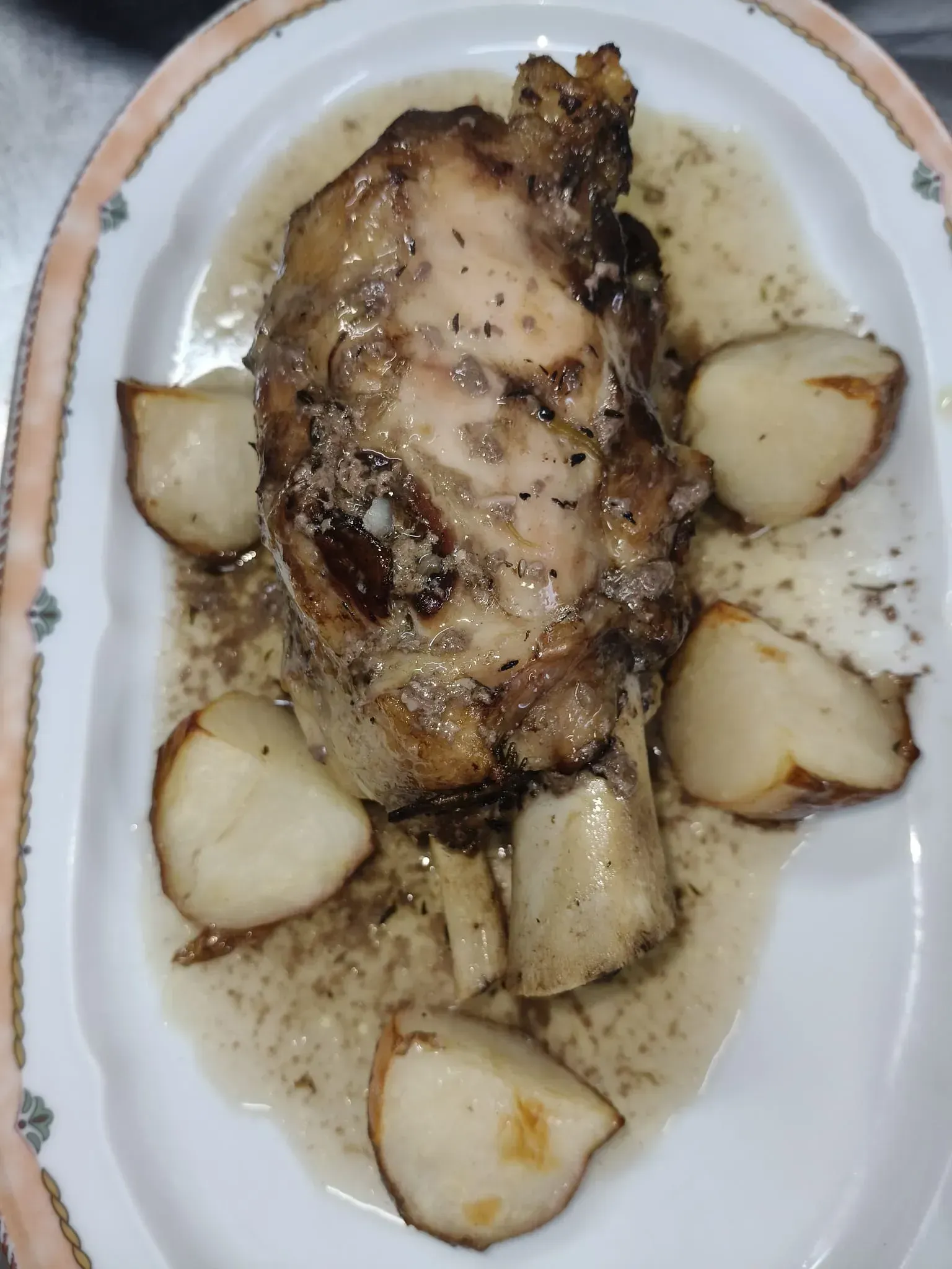Muslo de pollo asado con dientes de ajo asados ​​en un plato ovalado blanco.