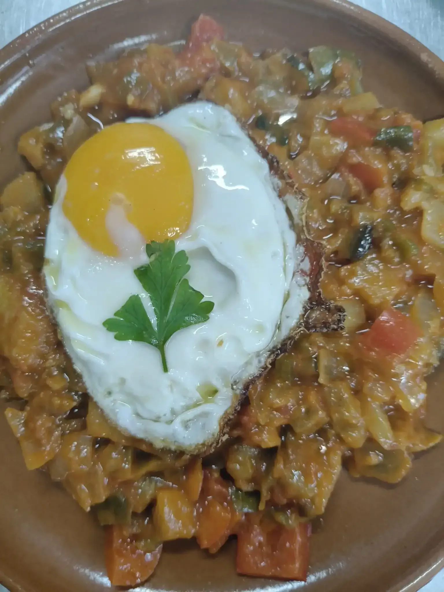 Verduras guisadas cubiertas con un huevo frito en un plato marrón.