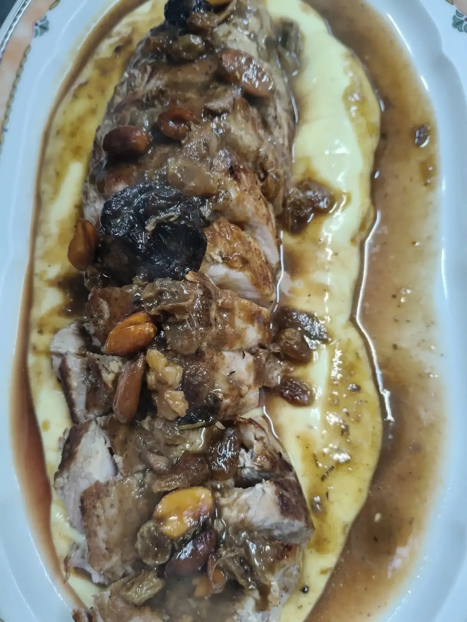 Solomillo de cerdo con salsa, pasas y almendras, servido sobre puré de papas en un plato blanco.