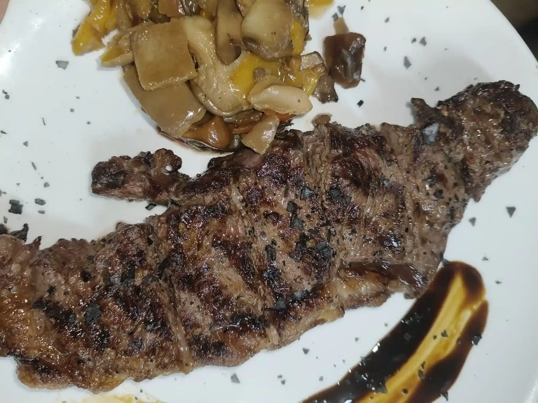 Bistec a la parrilla con verduras salteadas y salsa en un plato blanco.