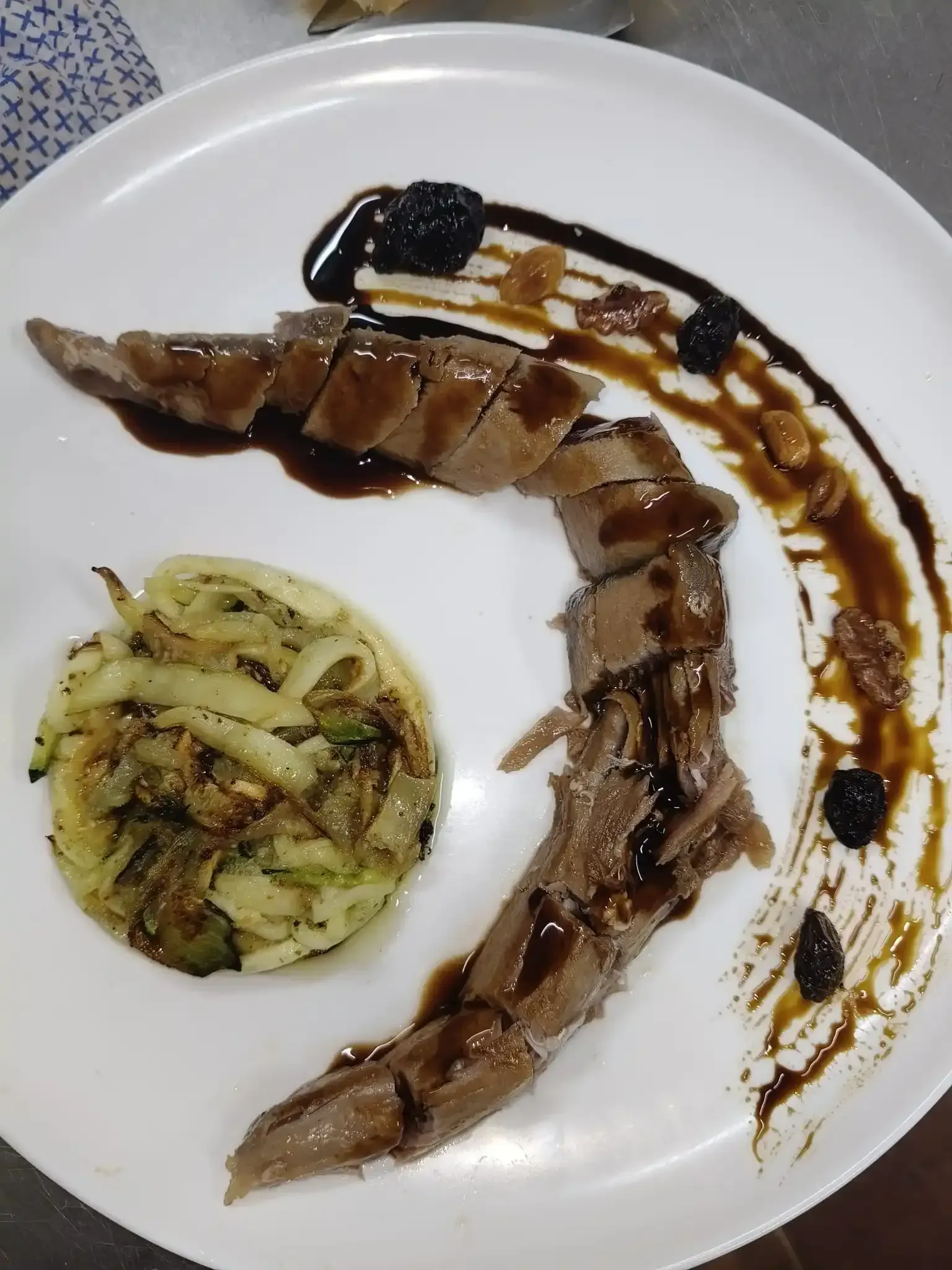 Carne en rodajas con salsa oscura, verduras cocidas y guarnición en un plato blanco.