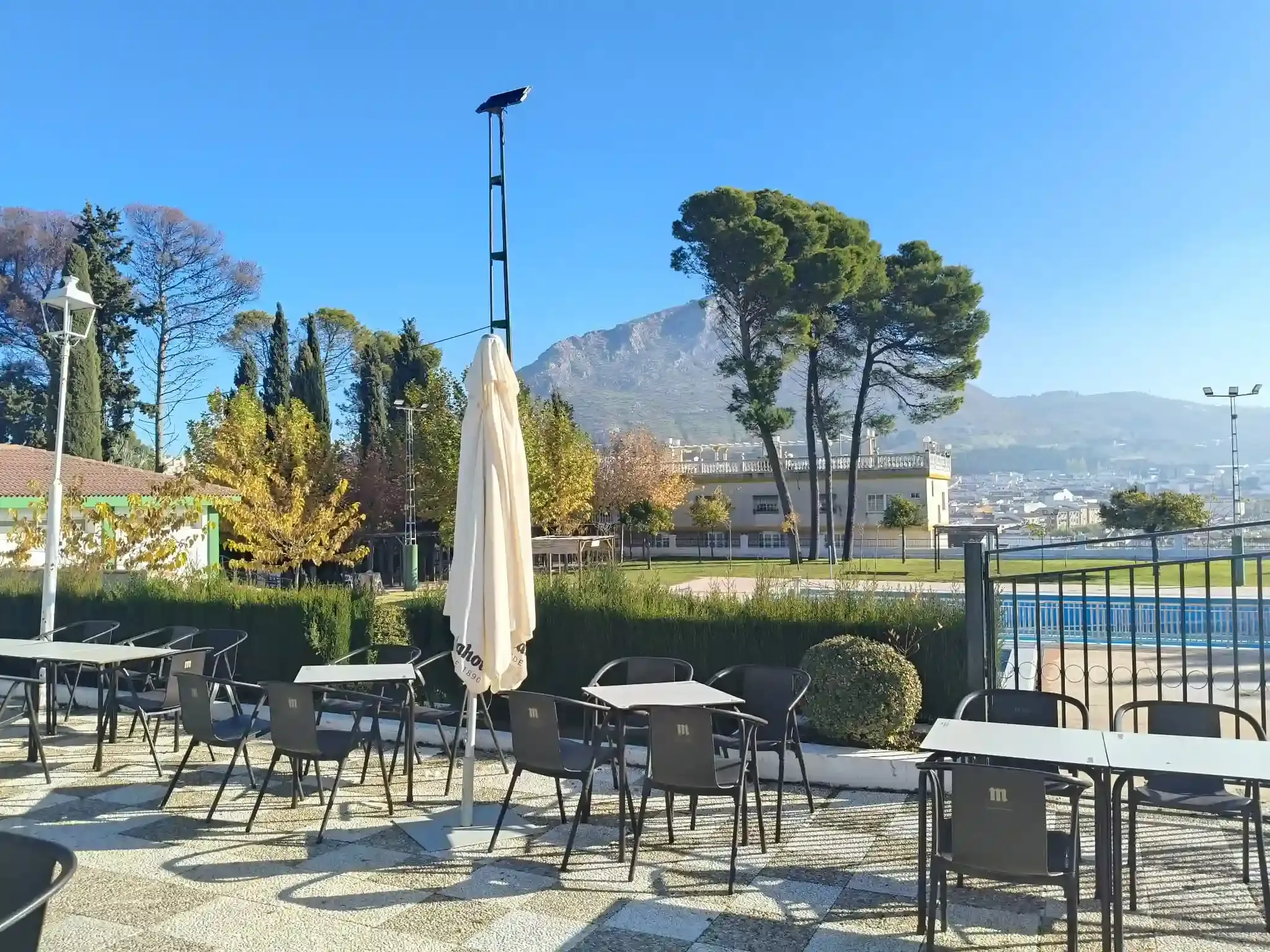 Mesas y sillas en un patio con piscina y montaña al fondo bajo un cielo azul.