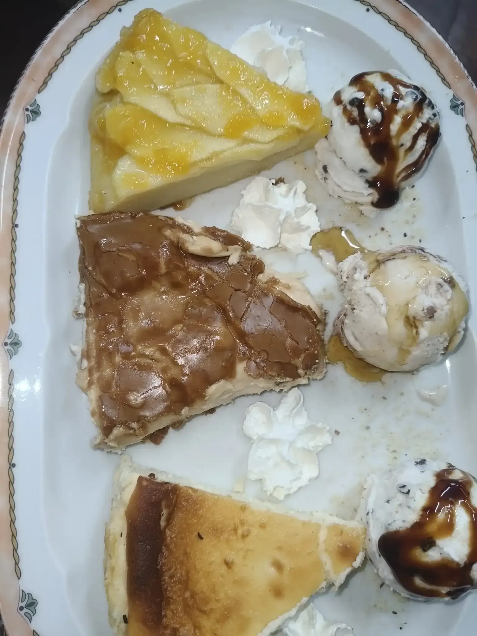 Plato ovalado con tarta de manzana, brownie, tarta de queso, crema batida y helado rociado con salsa.