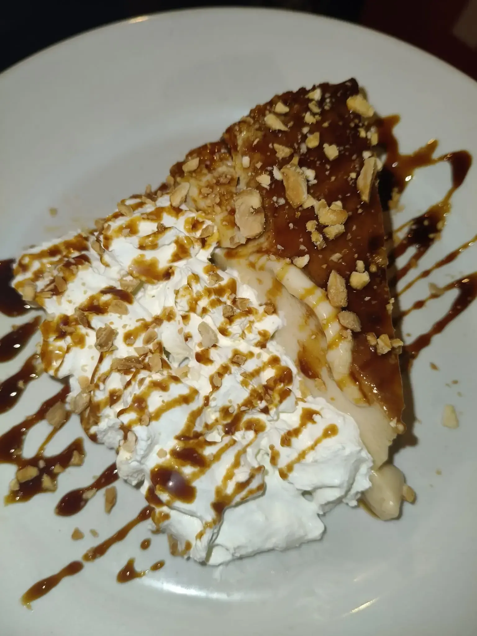 Rebanada de pastel de postre con crema batida, caramelo y nueces en un plato blanco.